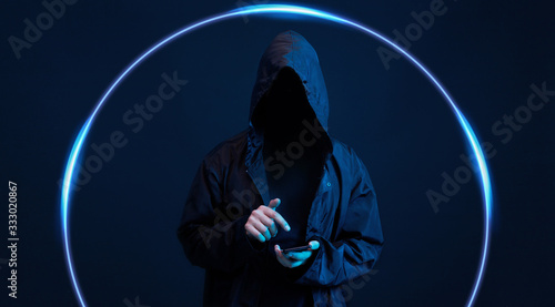 Dangerous hooded hacker with smartphone in his hand. Internet, cyber crime, cyber attack, system breaking and malware concept. Anonymous. Dark background. Black minimalism.