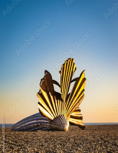 Foto Sculpture of a giant scallop on a pebble beach in setting sun