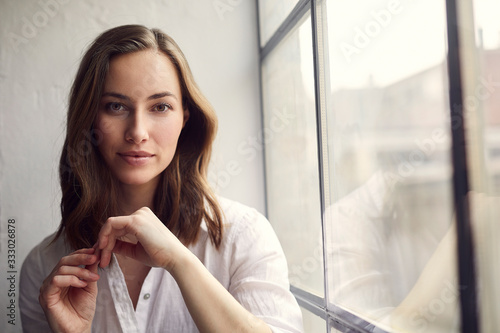 portrait of thoughtful pretty woman sitting in a window looking into the camera