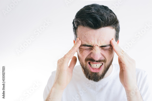 Picture of young bearded brunette man suffer from strong pain or headache. Hold fingers close to side of head. Need pill or medicine for relief. Isolated over background.