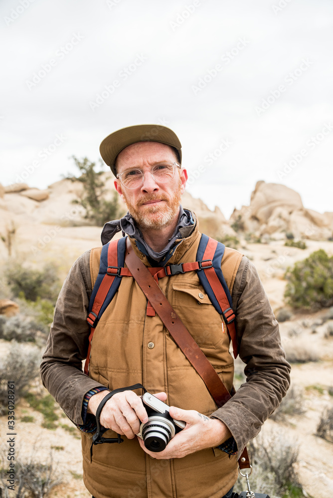 Focused mature man with camera and backpack in desert Focused mature man with camera and backpack in desert