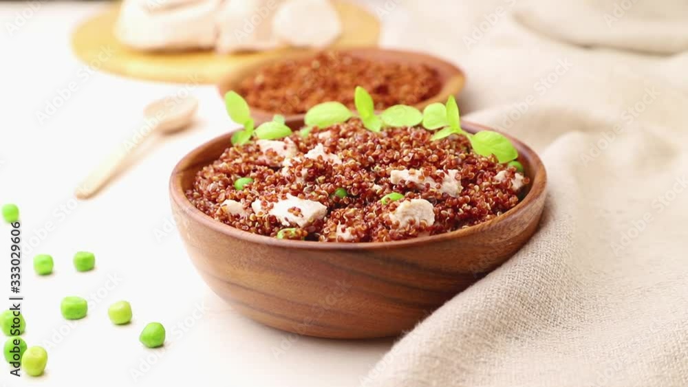 red quinoa porridge with green peas and chicken meat in wooden bowl decorate with microgreen basil sprouts. linen napkin, male hand. side view, close up. red quinoa porridge with green peas and chicken meat in wooden bowl decorate with microgreen basil sprouts. linen napkin, male hand. side view, close up.