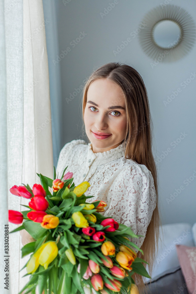 Beautiful young woman holds a multi-colored bouquet of tulips. Spring woman portrait. International Women's Day. Beautiful young woman holds a multi-colored bouquet of tulips. Spring woman portrait. International Women's Day.