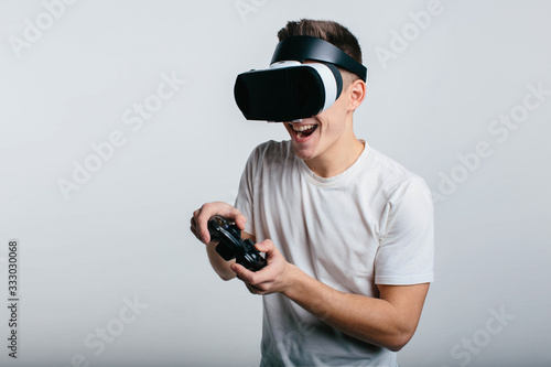 Man wearing virtual reality goggles and holding a gamepad while standing near white blackboard