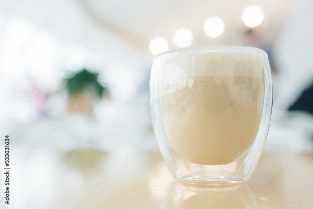 Cappuccino latte or coffee with milk in modern glass with double bottom. Close-up view. Reflection on glass. Blurred background. There is place for text. Cappuccino latte or coffee with milk in modern glass with double bottom. Close-up view. Reflection on glass. Blurred background. There is place for text.