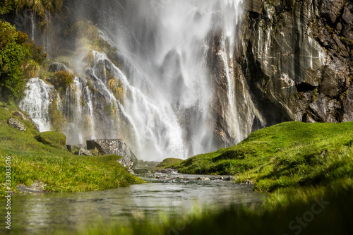 Waterfall cascading over rocks in a lush green grassy nature landscape © Cavan Images