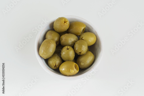Green olives in bowl close-up. Top view on white background. A delicious and healthy ingredient for olive oil, pizza, and vegetarians