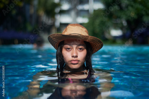 Stylish trendy young teen visco girl in the pool wearing a straw hat