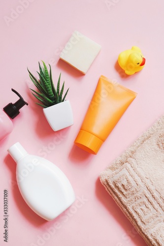 liquid soap, white shampoo bottle, orange cream tube, aloe vera, yellow rubber duck and beige cotton towel on a pink background. Hair and skin care cosmetic products. Flat lay beauty photography