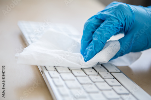 Coronavirus Epidemic Outbreak. Close-up of hand in protective glove using wet wipe to disinfect a computer keyboard.  photo