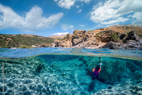 A over-and-under photograph of a free diver girl with the amazing landscape and a cloudy sky. А spectacularly clear waters.