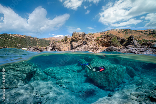 A over-and-under photograph of a free diver girl with the amazing landscape and a cloudy sky. А spectacularly clear waters.