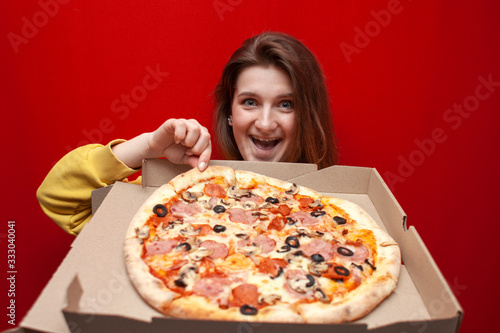 young happy hungry girl eats fresh pizza from a box on a colored background, a student takes a slice of pizza from a box