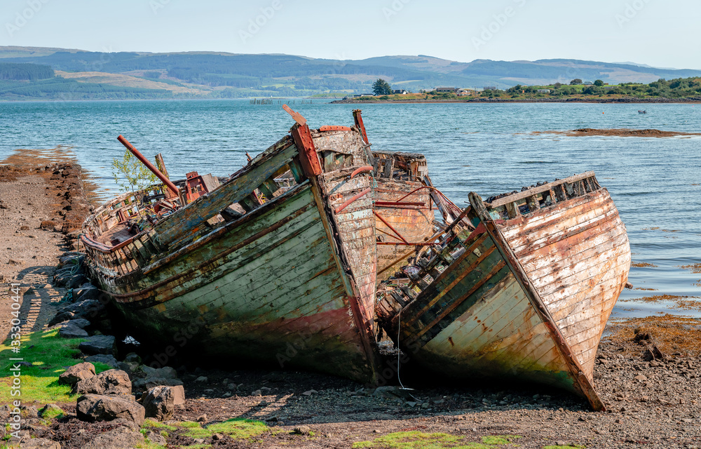 Beautiful seascape with three semi-destroyed old fishing boat in the beach and the Sound of Mull in the background. Isle of Mull, Scotland, August 2019.