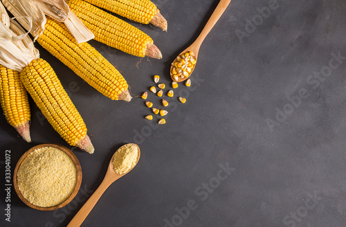 Corn flour in wooden bowl and spoon with dried corn groats, kernels on rustic table. corn ingredients concept