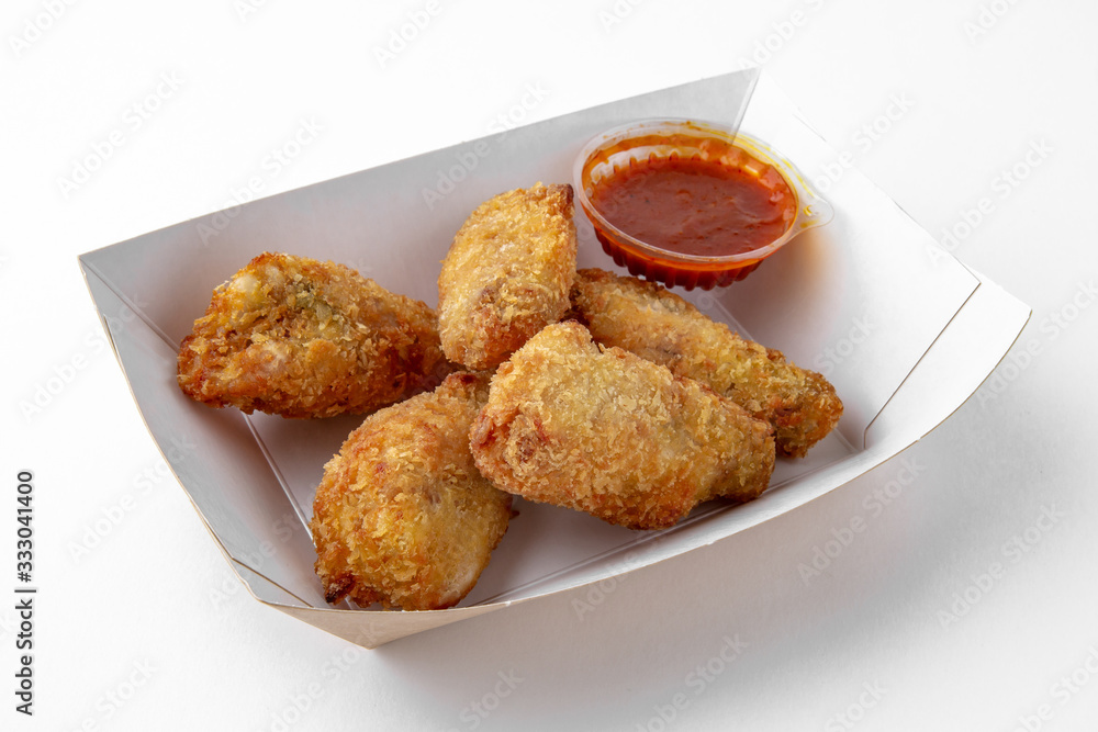 Chicken wings or drumsticks in a crispy batter with sauce in a paper plate for take away or food delivery isolated on a white background. Chicken wings or drumsticks in a crispy batter with sauce in a paper plate for take away or food delivery isolated on a white background.