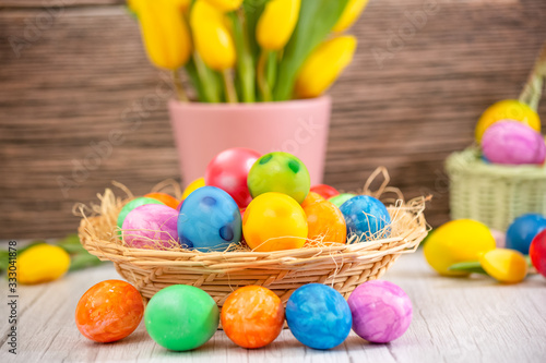 Beautiful group Easter eggs in the spring of easter day, red eggs, blue, purple and yellow in Wooden basket with tulips on the  wood table background