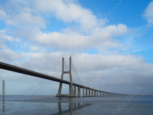 Bridge Vasco de Gama Lisbon crossing the river Tejo reflected in the water on a cloudy day. © Ombres