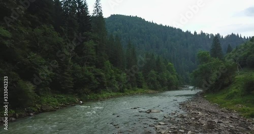 Moving forward and getting higher above a river in the forest mountain valley.