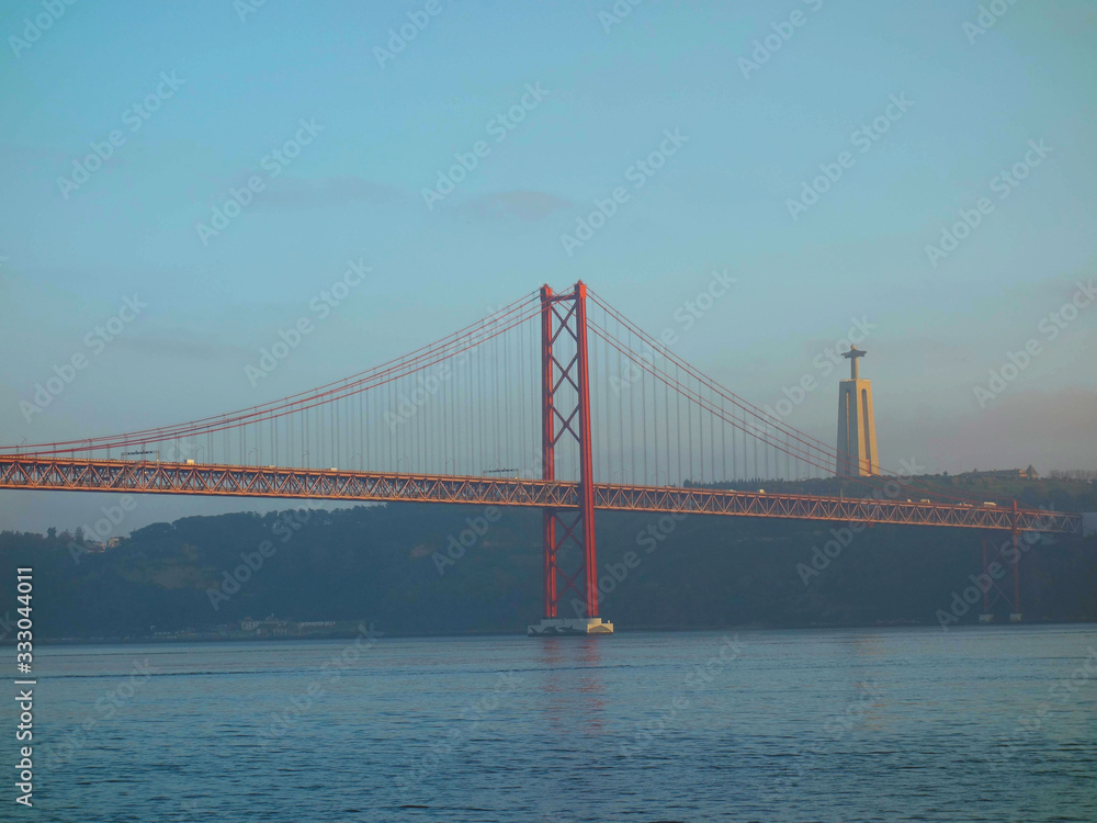 Lisbon, Portugal-23 December 219: skyline, red bridge on 25 April crossing the river Tejo on a cloudy day at dusk in the background Christ the King.