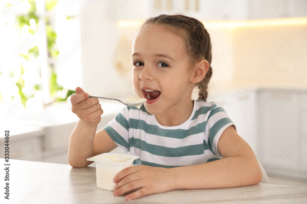 Cute little girl eating tasty yogurt at table in kitchen Cute little girl eating tasty yogurt at table in kitchen