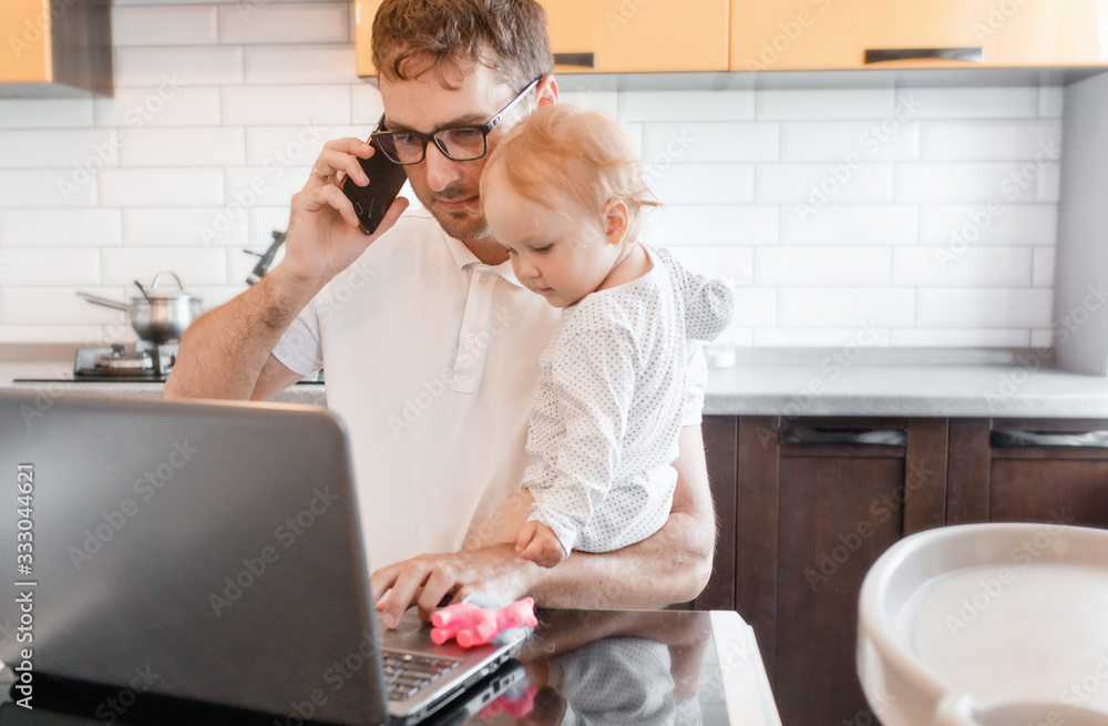 Handsome young man working at home with a laptop with a baby on his hands. Stay home concept. Home office with kids. Handsome young man working at home with a laptop with a baby on his hands. Stay home concept. Home office with kids.