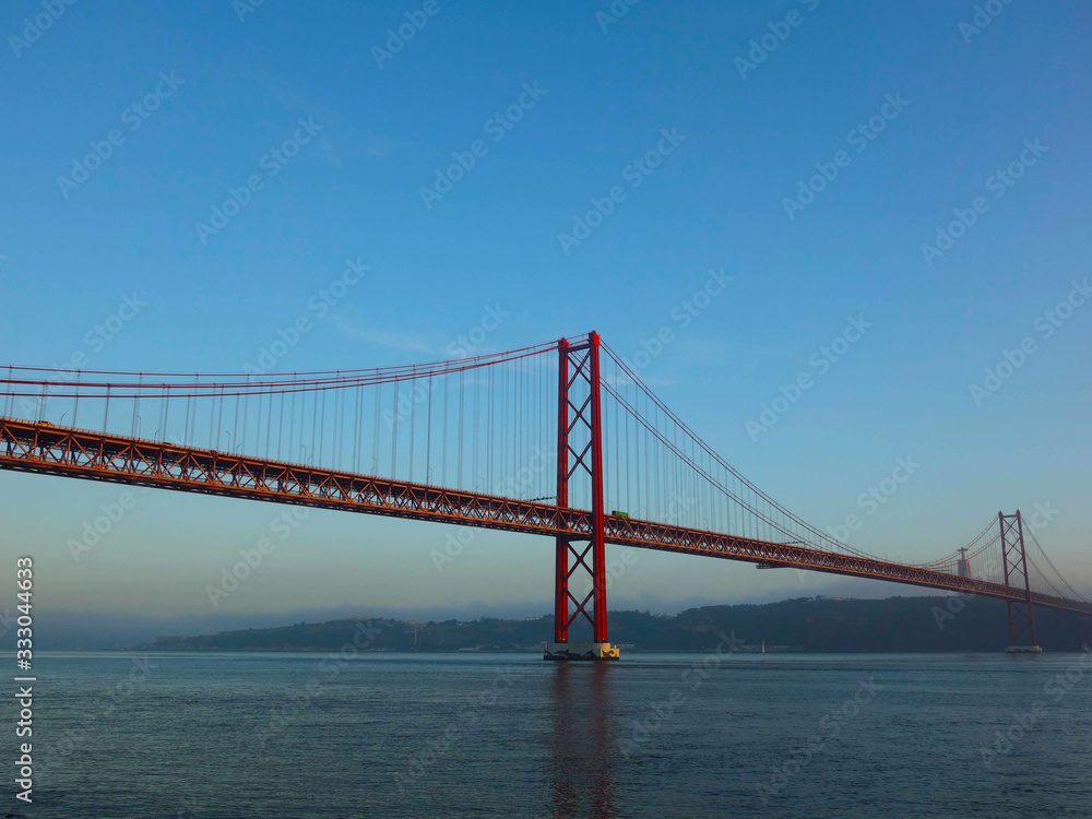 Lisbon, Portugal-23 December 219: skyline, red bridge on 25 April crossing the river Tejo on a cloudy day at dusk in the background Christ the King.