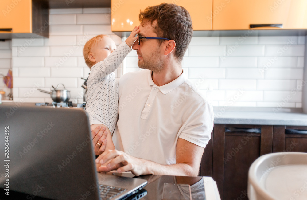 Handsome young man working at home with a laptop with a baby on his hands. Stay home concept. Home office with kids. Handsome young man working at home with a laptop with a baby on his hands. Stay home concept. Home office with kids.