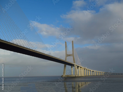 The Vasco de Gama Lisbon bridge crosses the river Tejo and reflects on the water illuminated by a ray of sunshine.
