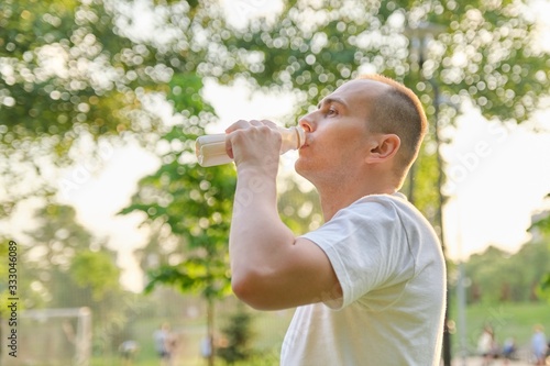 Middle-aged man drinking milk, dairy product from bottle outdoor