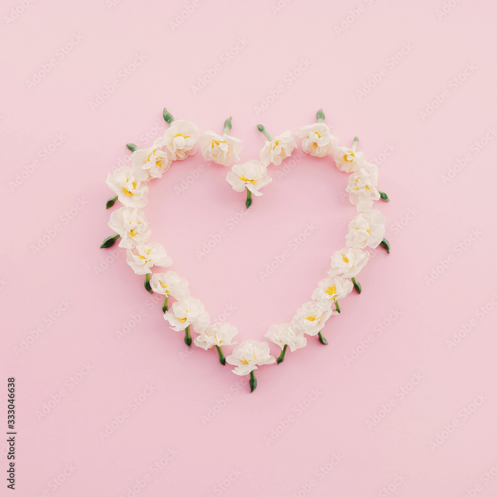 Floral heart made of fresh daffodil flowers on pastel pink background.