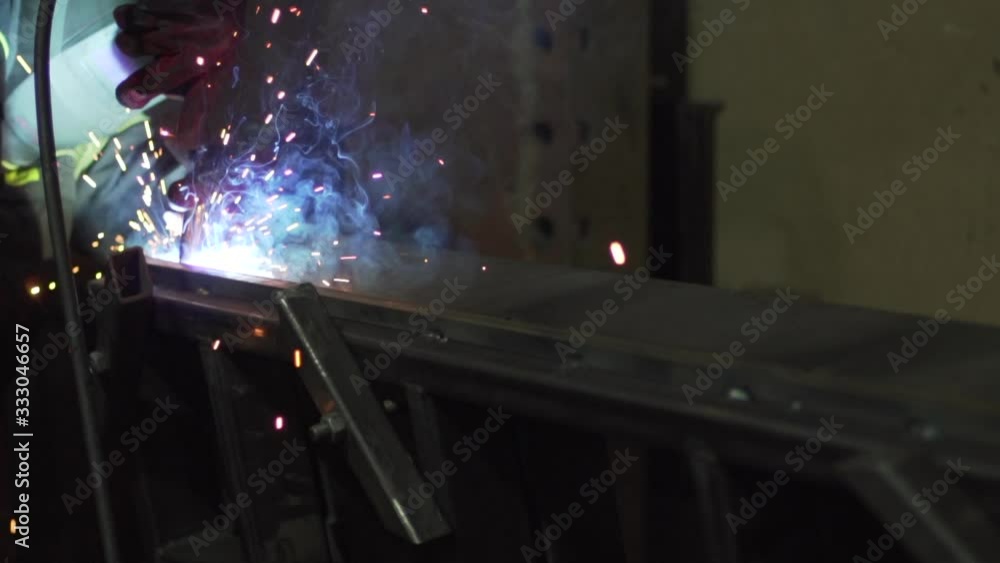 A welder welds metal parts using a welding machine. Detailed close-up. A welder welds metal parts using a welding machine. Detailed close-up.