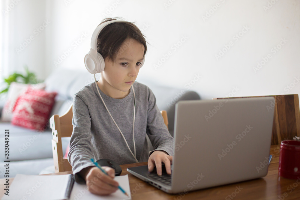 School child, sitting at the table with laptop, writing school tasks while homeschooling School child, sitting at the table with laptop, writing school tasks while homeschooling