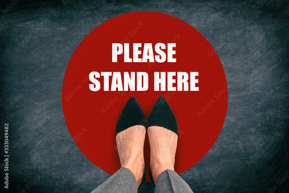 COVID-19 Coronavirus message asking supermarket customer to stand in space. Top view of feet standing in red circle with text in public space practicing social distancing. Blackboard background. - obrazy, fototapety, plakaty 