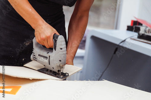 A young man cuts a pattern on plywood with an electrical fretsaw