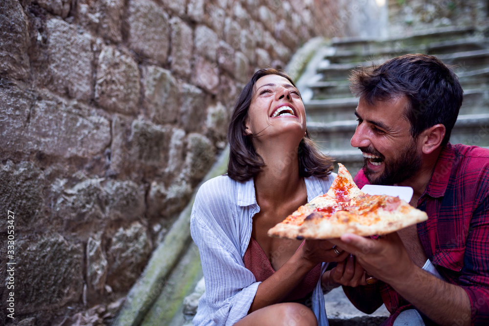 Smiling love couple eating pizza at street