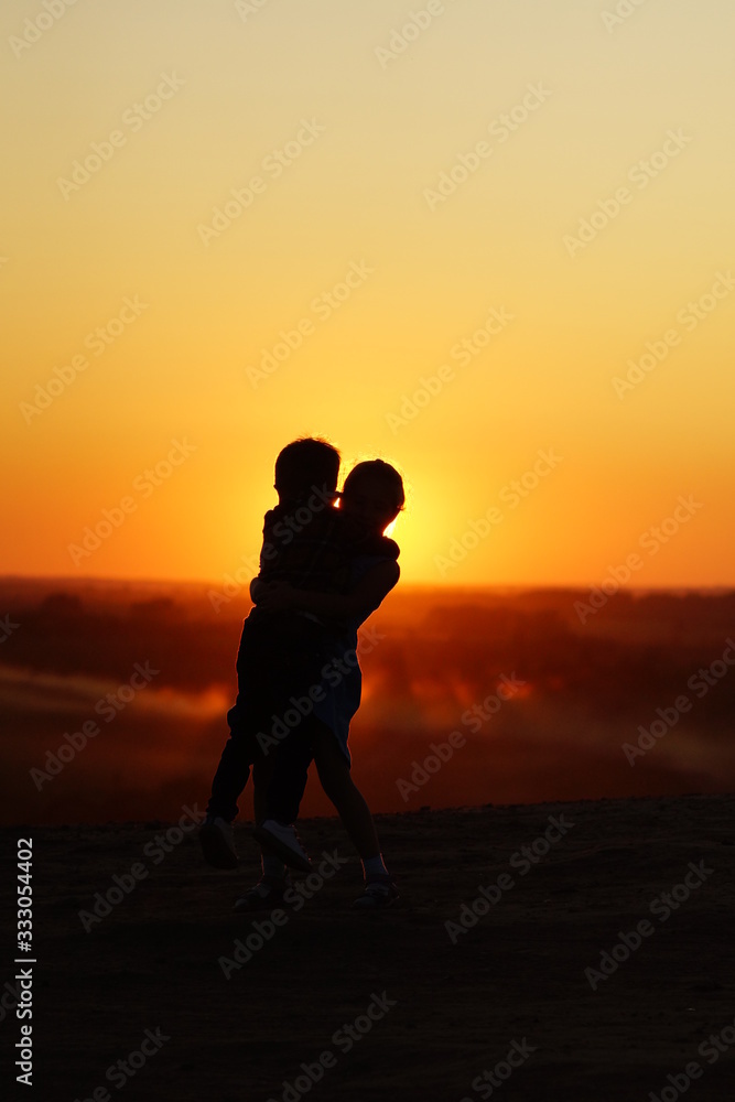 Silhouette of a girl and a boy on top of mountain at sunset. Children's hugs.
