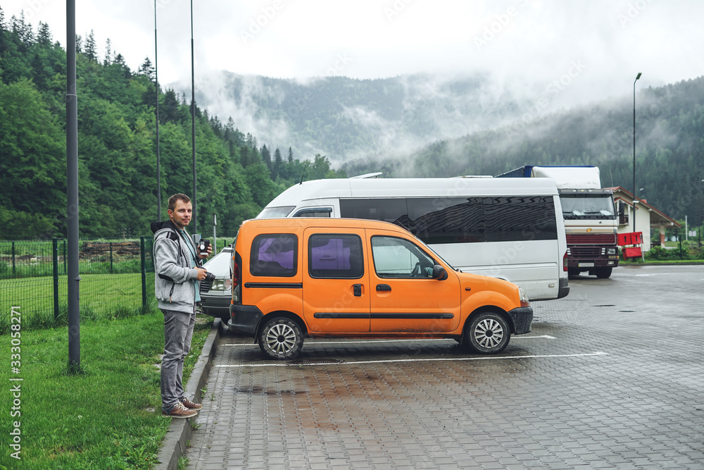 Fototapeta premium The guy in a sports suit near the orange car. Man on mountains background.