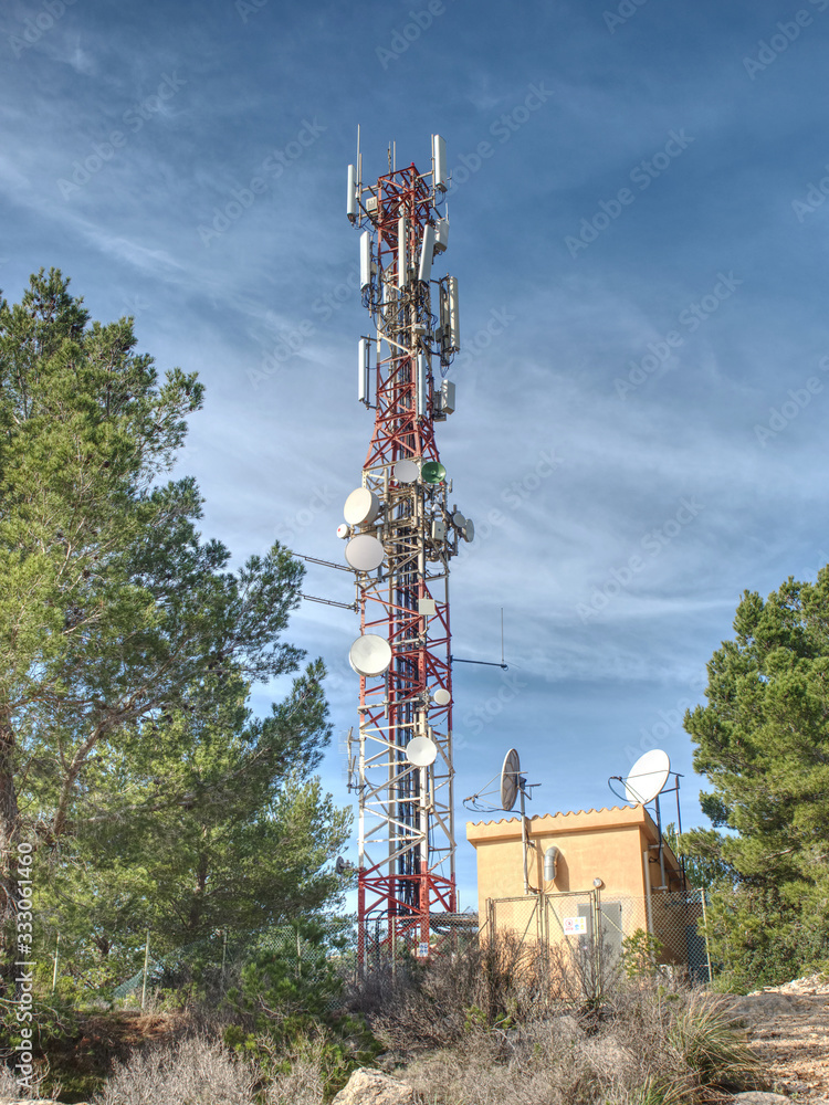 Modern tower with huge complex of telecommunication antennas on old bricks house hidden in pine trees.  Mountain trail over Pintal Vermell peak, Mallorka island, Spanish  Balears islands.