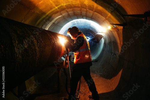 Worker in protective mask welding pipe in tunnel photo