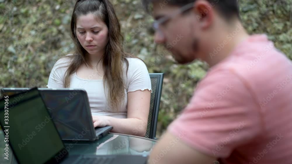 Extreme closeup on high school girl in focus and college boy doing school work on their laptops outside while on lock down from coronavirus. Extreme closeup on high school girl in focus and college boy doing school work on their laptops outside while on lock down from coronavirus.