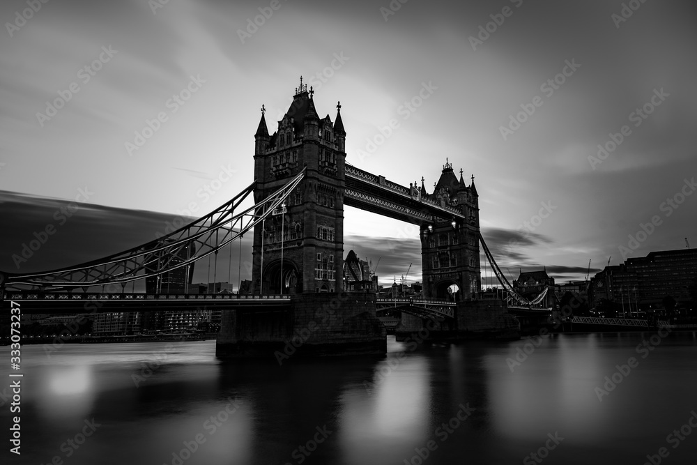 Tower Bridge located in London city, United Kingdom with gray, grey scale view. Calm River Thames in long exposure shot with tourism, tourist view in city landscape	