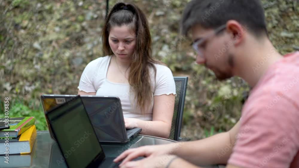 Closeup on high school girl in focus and college boy doing school work on their laptops outside while on lock down from coronavirus. Closeup on high school girl in focus and college boy doing school work on their laptops outside while on lock down from coronavirus.