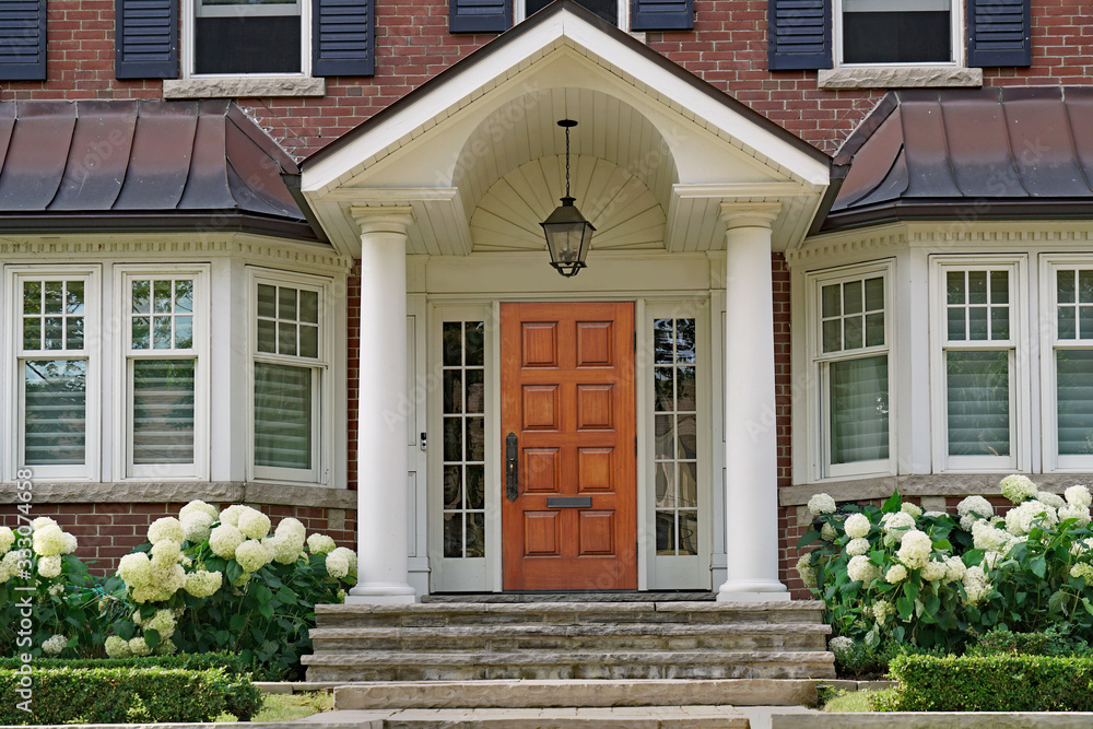 Front door of traditional two story house with portico entrance and hydrangea flowers