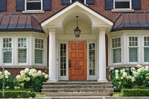 Front door of traditional two story house with portico entrance and hydrangea flowers © Spiroview Inc.