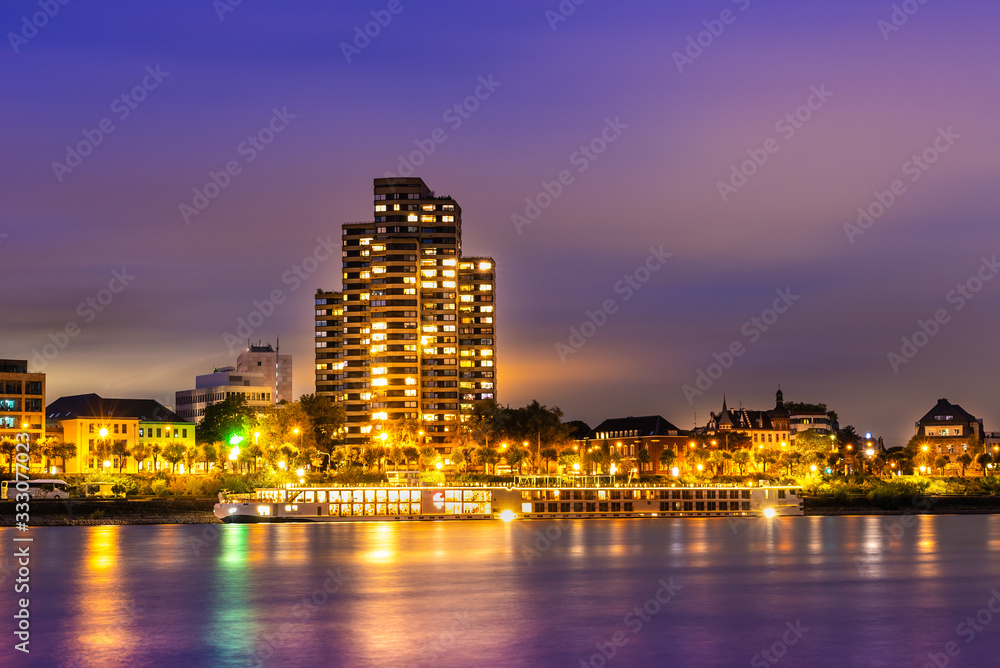 Buildings by the Rhine in Germany at night; cruise ship sailing on the river