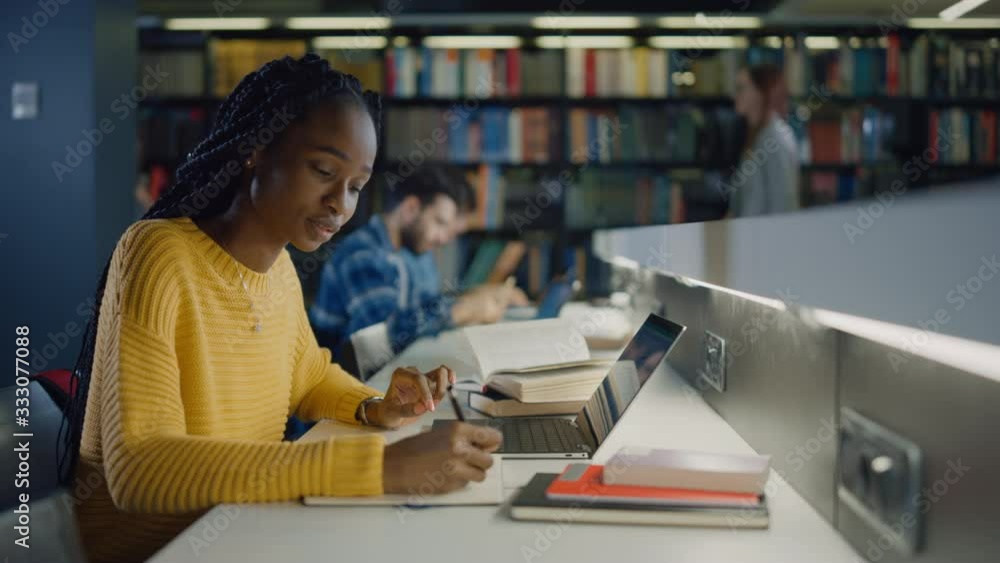 University Library: Gifted Black Girl uses Laptop, Writes Notes for the Paper, Essay, Study for Class Assignment. Diverse Multi-Ethnic Group of Students Learning, Studying for Exams, Talk in College University Library: Gifted Black Girl uses Laptop, Writes Notes for the Paper, Essay, Study for Class Assignment. Diverse Multi-Ethnic Group of Students Learning, Studying for Exams, Talk in College