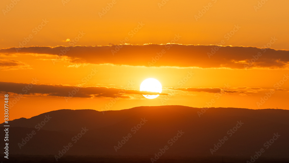 Silhouette of sun in orange sky and mountains at sunset; natural landscape