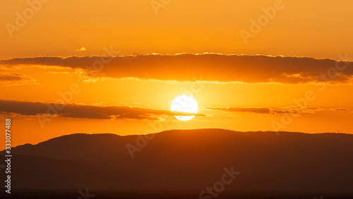 Silhouette of sun in orange sky and mountains at sunset; natural landscape