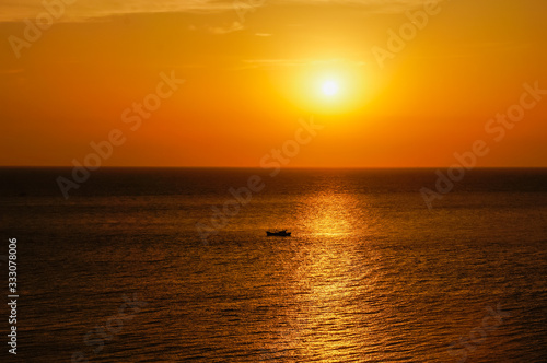 A beautiful scenery of a ship sailing in the calm sea under an orange sky over the sunset